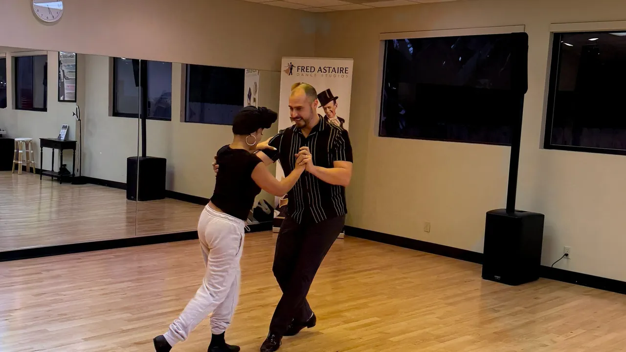 Two adults smile while practicing partner dancing on the studio floor.